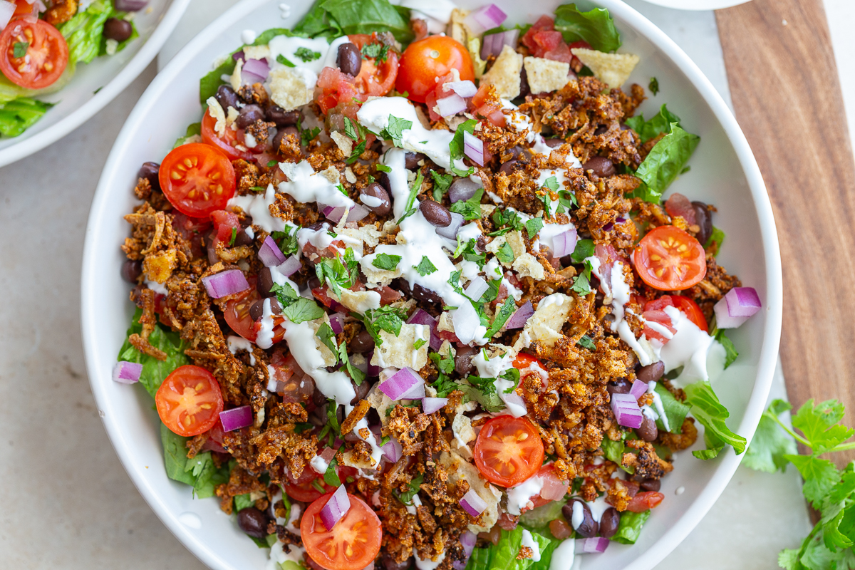 taco tofu rice bowls that is a large bowl of lettuce topped with rice, cherry tomatoes, crispy tofu taco meat, and drizzled with sour cream
