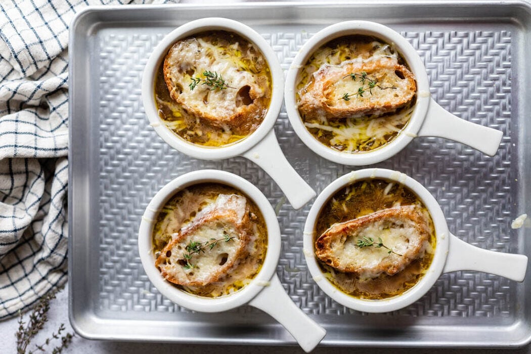 bowls of french onion soup sitting on a baking sheet with bread and melted cheese on top