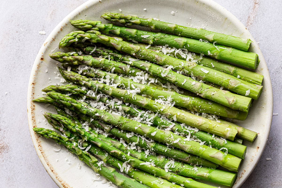 Cooked asparagus on a plate with a sprinkle of parmesan cheese.