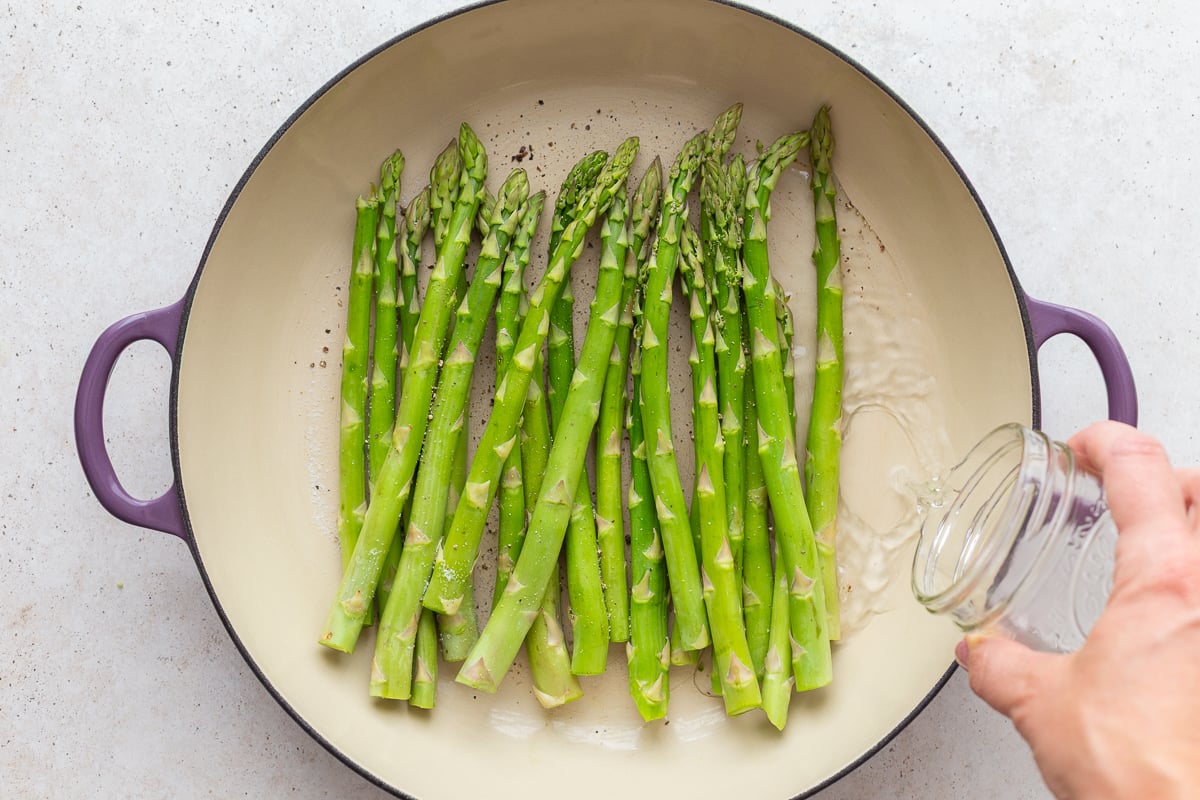 asparagus in a large skillet with water being poured in