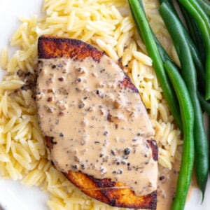 tofu "steak" laying on a bed of orzo, next to green beans, and covered in a creamy peppercorn sauce