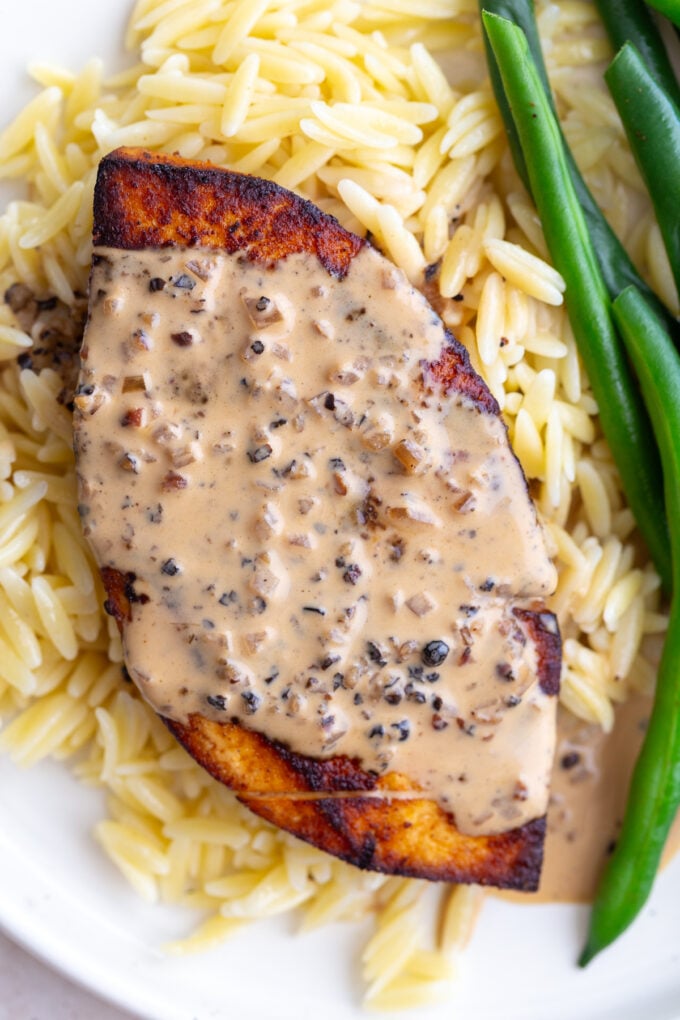 tofu "steak" laying on a bed of orzo, next to green beans, and covered in a creamy peppercorn sauce