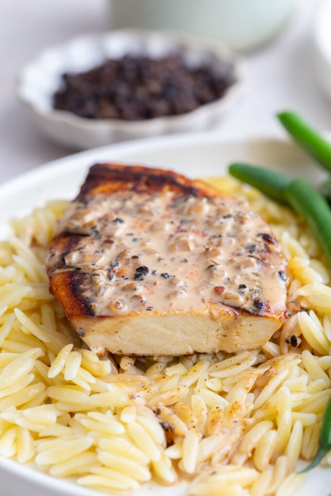 tofu "steak" laying on a bed of orzo, next to green beans, and covered in a creamy peppercorn sauce