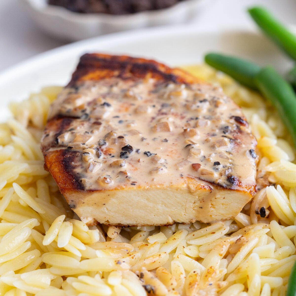 tofu "steak" laying on a bed of orzo, next to green beans, and covered in a creamy peppercorn sauce