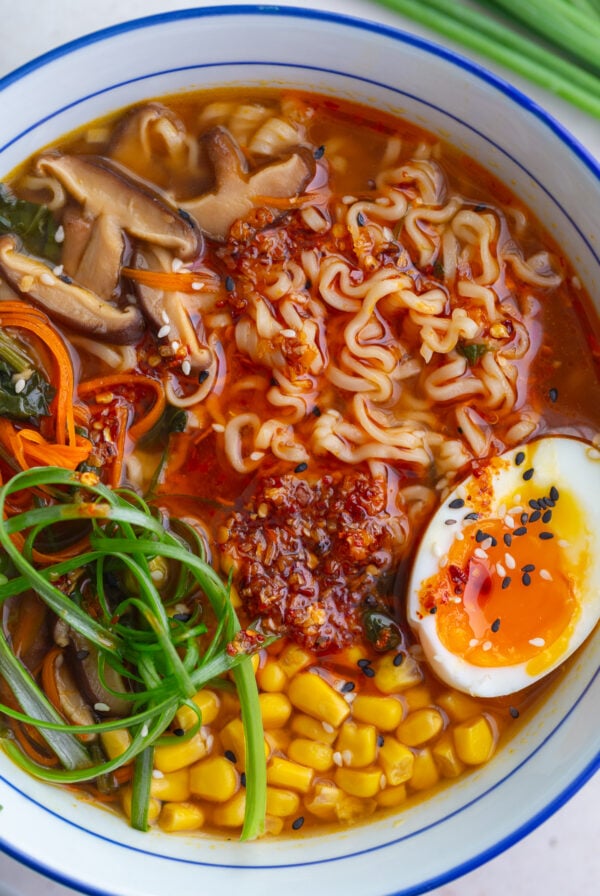 easy homemade ramen in a large ramen bowl. the ramen is topped with a soft boiled egg, green onions, corn, and sesame seeds