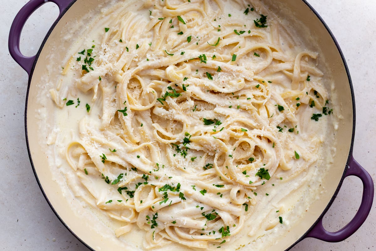 homemade fettuccini alfredo sauce in a large skillet topped with fresh herbs