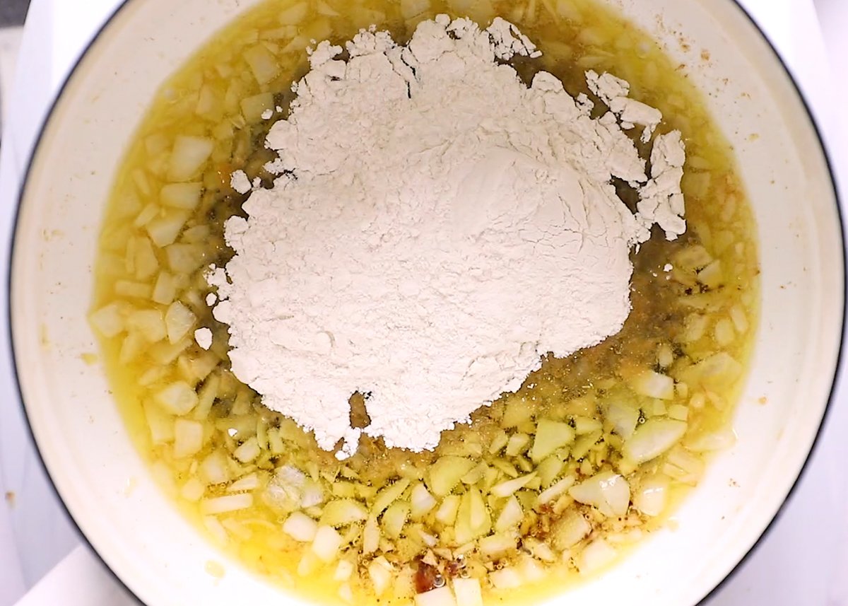 making vegan gravy with onion and oil in a pan and flour being poured in