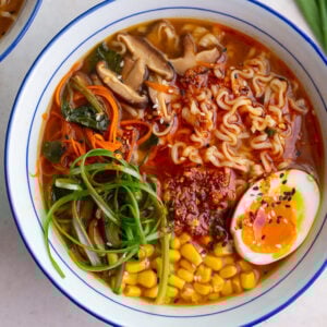 easy homemade ramen in a large ramen bowl. the ramen is topped with a soft boiled egg, green onions, corn, and sesame seeds