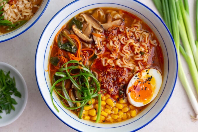 easy homemade ramen in a large ramen bowl. the ramen is topped with a soft boiled egg, green onions, corn, and sesame seeds