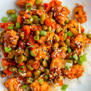 gochujang tofu and edamame stir fry in a large white bowl topped with sesame seeds
