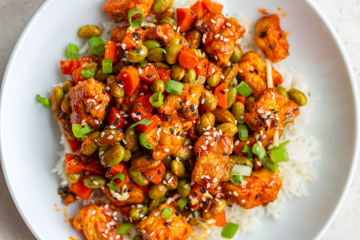 gochujang tofu and edamame stir fry in a large white bowl topped with sesame seeds