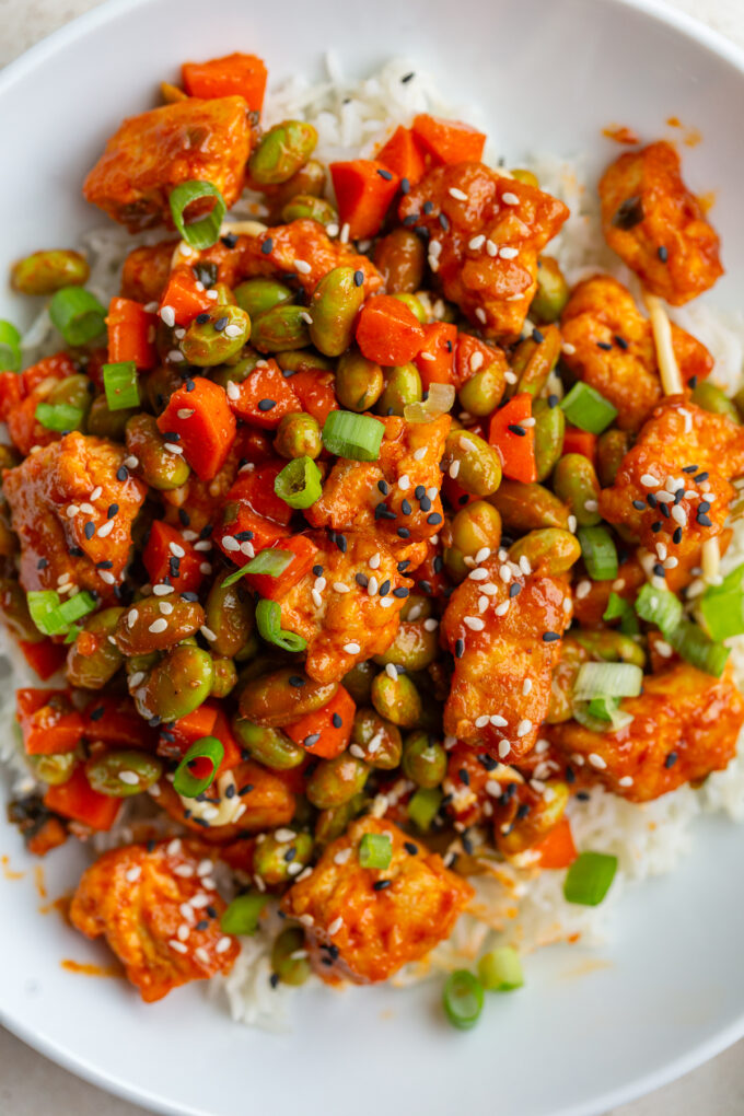 gochujang tofu and edamame stir fry in a large white bowl topped with sesame seeds
