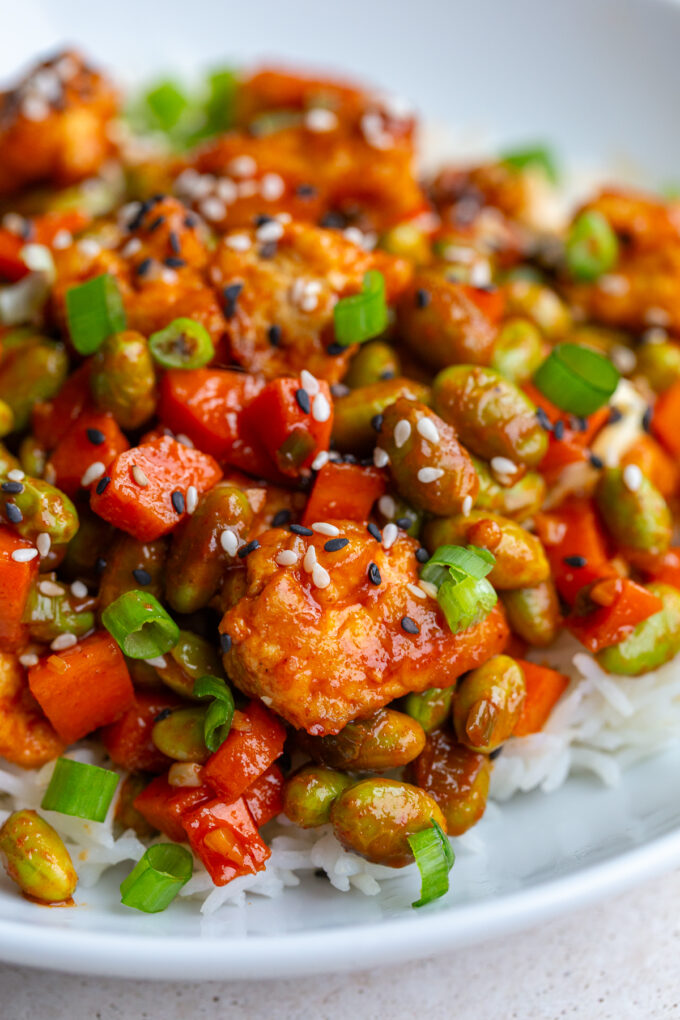 gochujang tofu and edamame stir fry in a large white bowl topped with sesame seeds