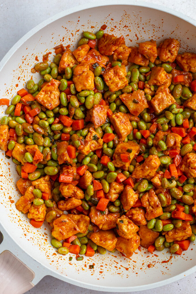 gochujang tofu and edamame stir fry in a large white skillet topped with sesame seeds
