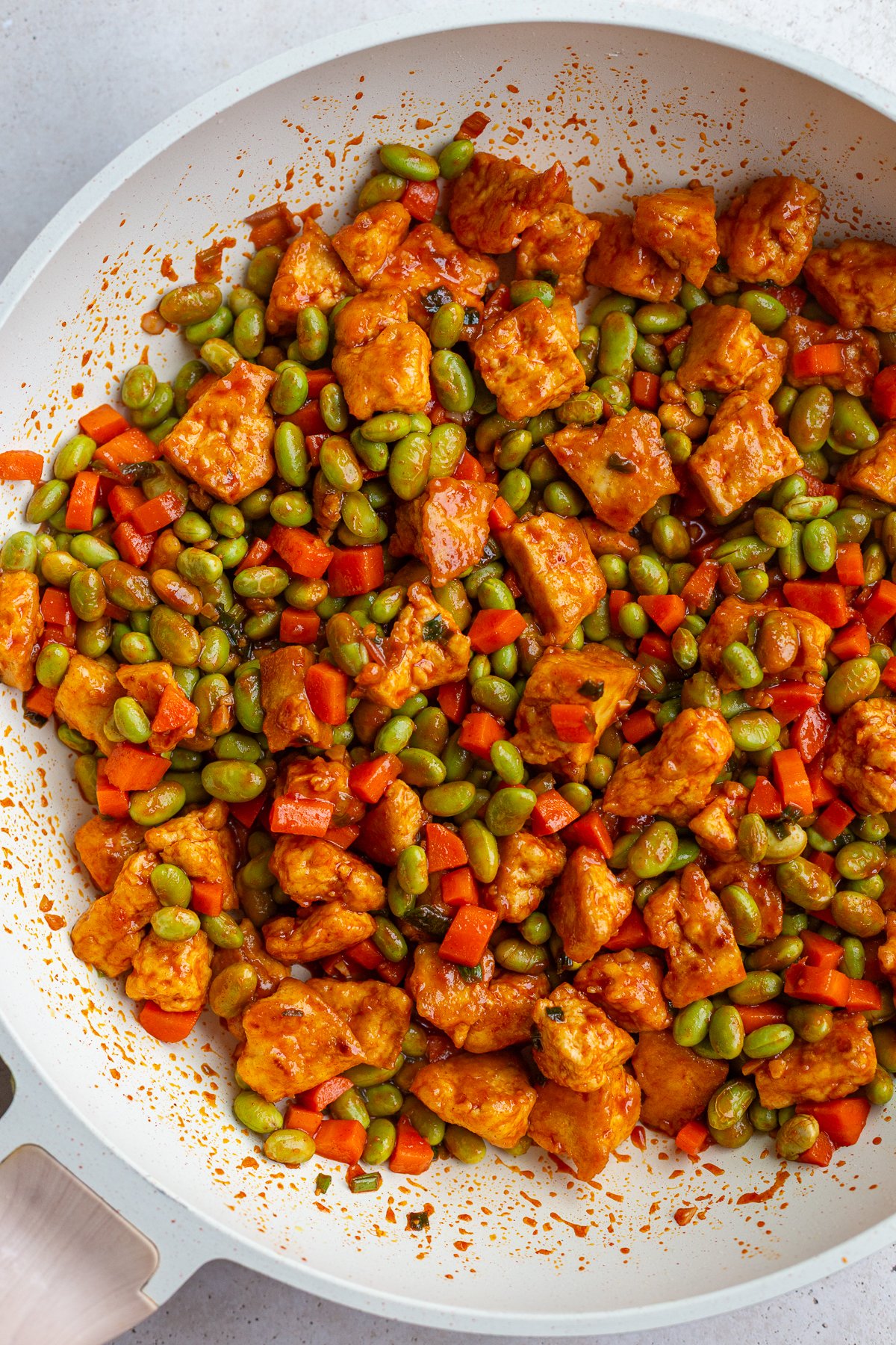 gochujang tofu and edamame stir fry in a large white skillet topped with sesame seeds