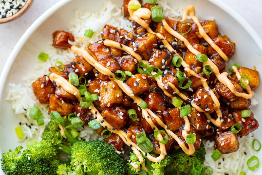honey garlic tofu drizzled with bang bang sauce on a bed of rice with broccoli next to it