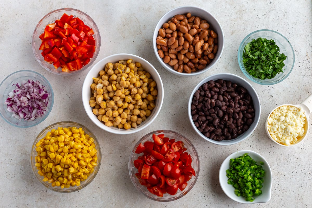 ingredients needed for southwestern bean salad including chickpeas, pinto beans, black beans, bell pepper, cherry tomatoes, jalapeno, corn and bell pepper