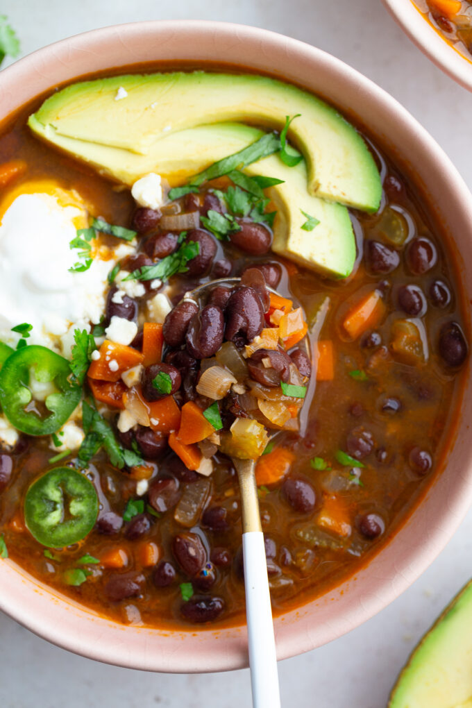 spicy black bean soup in a pink bowl topped with avocado, sour cream, cheese, and cilantro
