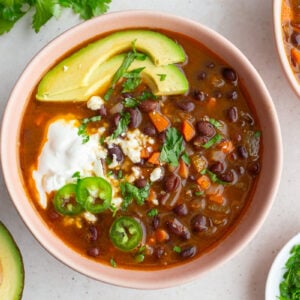 spicy black bean soup in a pink bowl topped with avocado, sour cream, cheese, and cilantro
