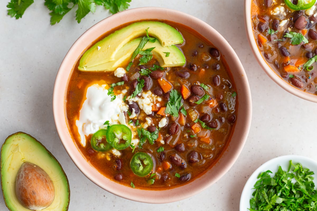 spicy black bean soup in a pink bowl topped with avocado, sour cream, cheese, and cilantro