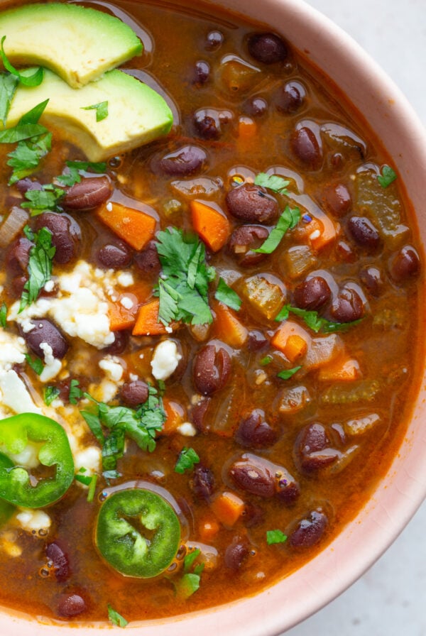 spicy black bean soup in a pink bowl topped with avocado, sour cream, cheese, and cilantro