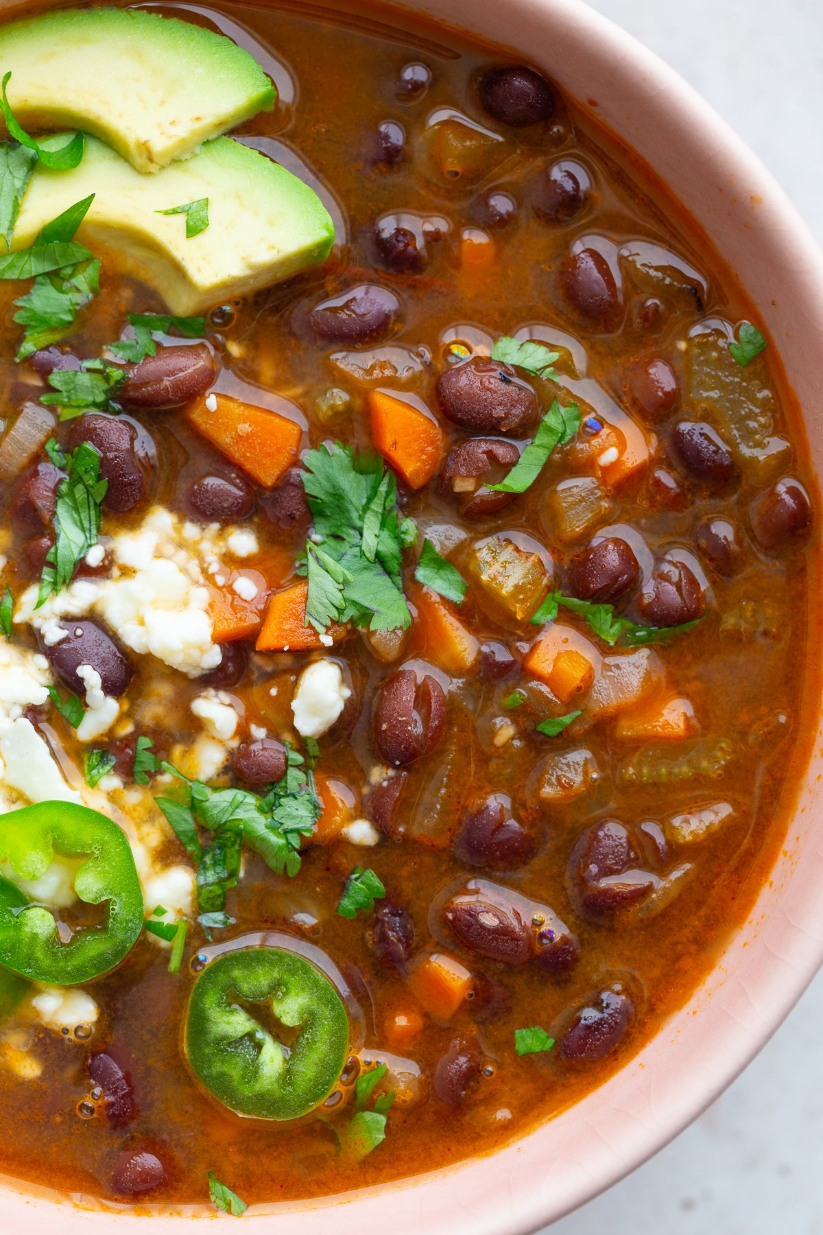 spicy black bean soup in a pink bowl topped with avocado, sour cream, cheese, and cilantro