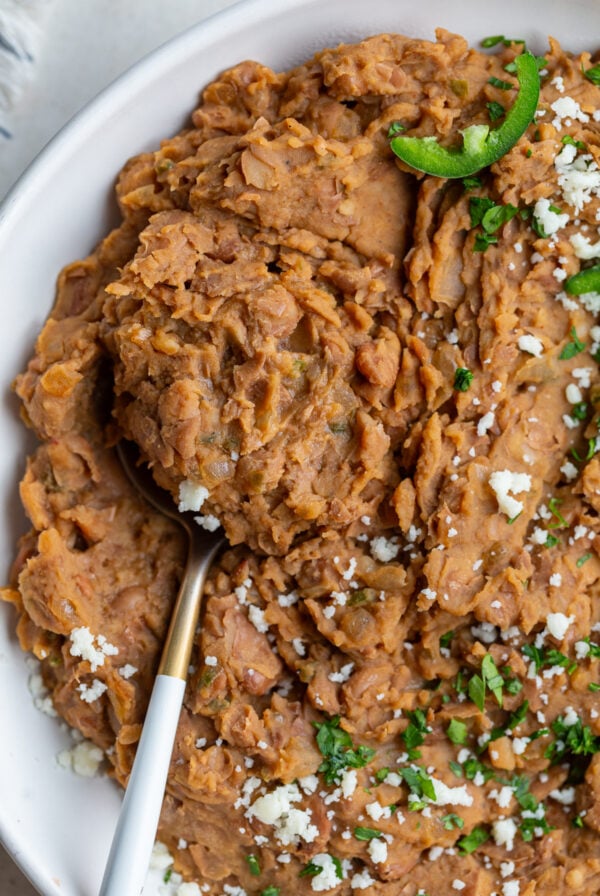 up close shot of homemade refried beans with a spoon in the side and fresh jalapenos