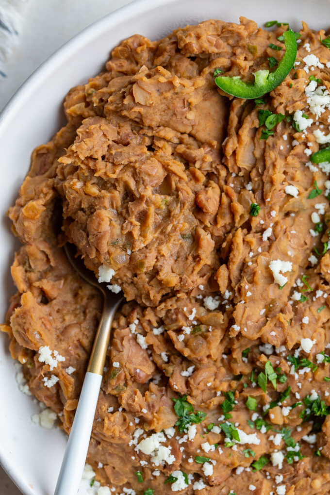 up close shot of homemade refried beans with a spoon in the side and fresh jalapenos