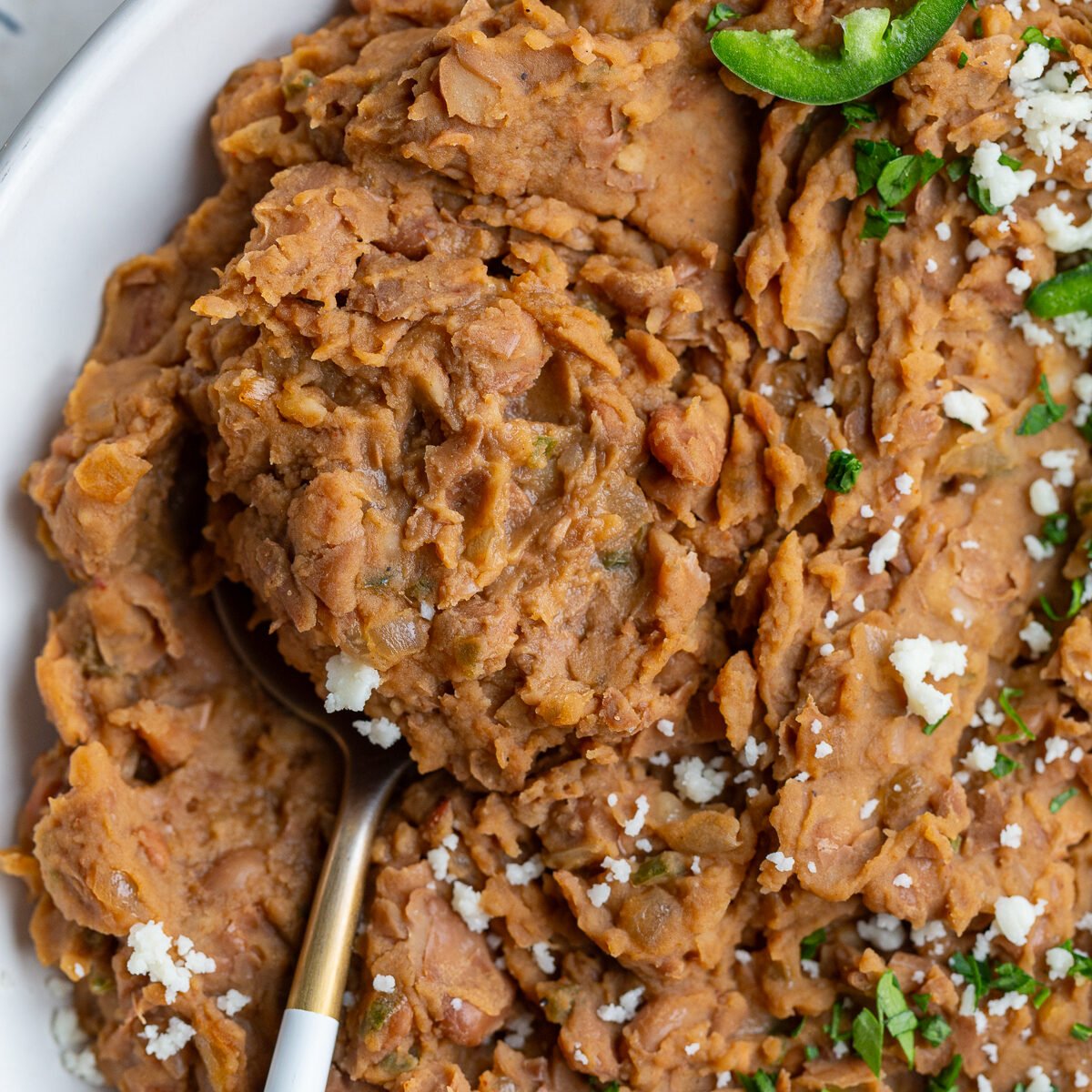 up close shot of homemade refried beans with a spoon in the side and fresh jalapenos