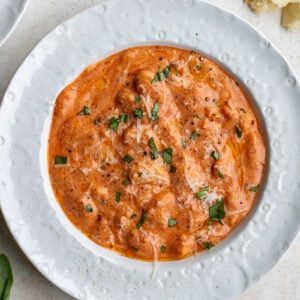 vodka sauce butter beans on a white bowl topped with basil and parmesan cheese