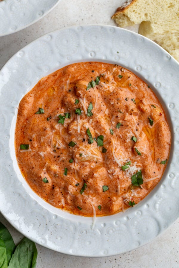 vodka sauce butter beans on a white bowl topped with basil and parmesan cheese