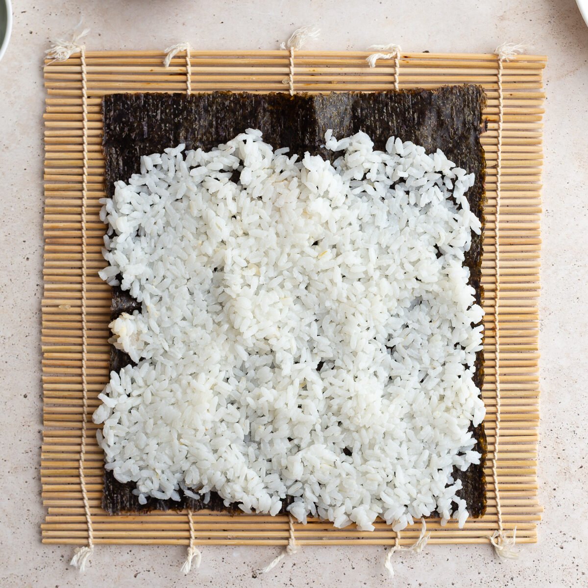 Topping a nori sheet that is on a sushi mat with rice.