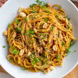 peanut butter noodles with peanuts and green onion in a white bowl