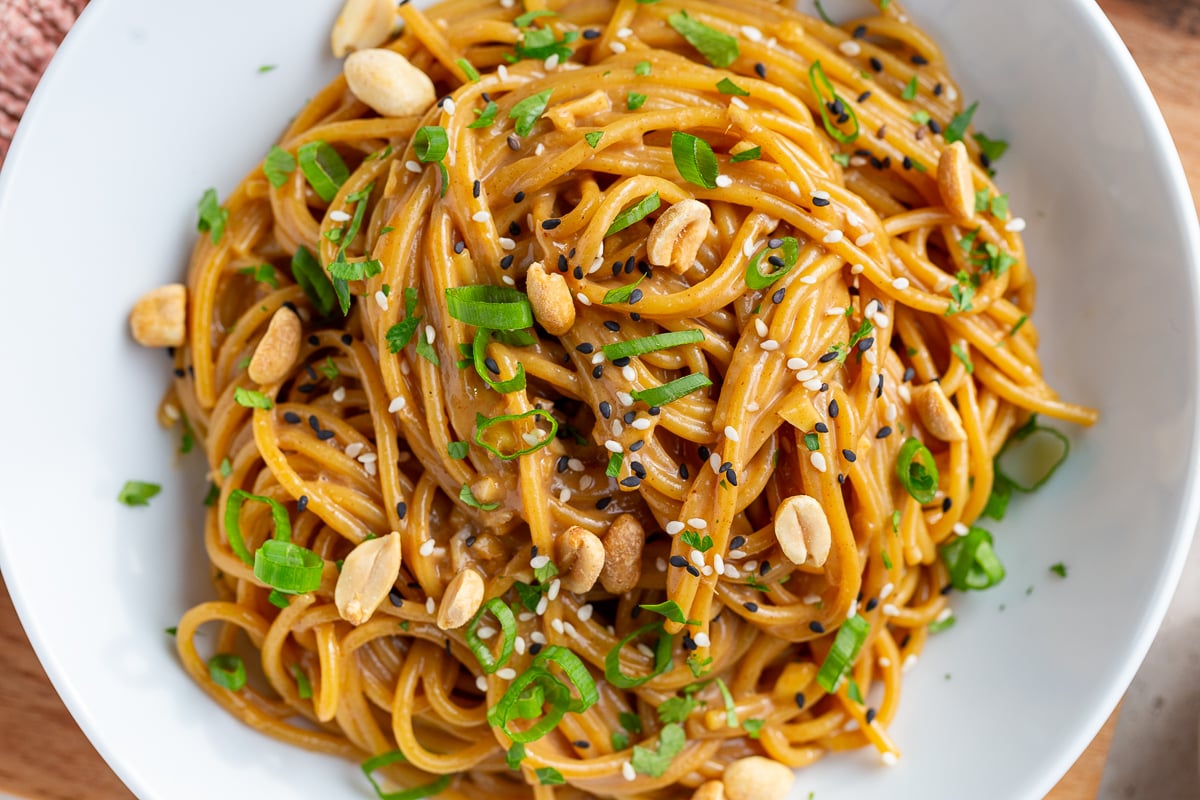 peanut butter noodles with peanuts and green onion in a white bowl