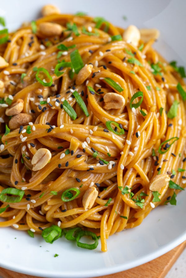 peanut butter noodles with peanuts and green onion in a white bowl