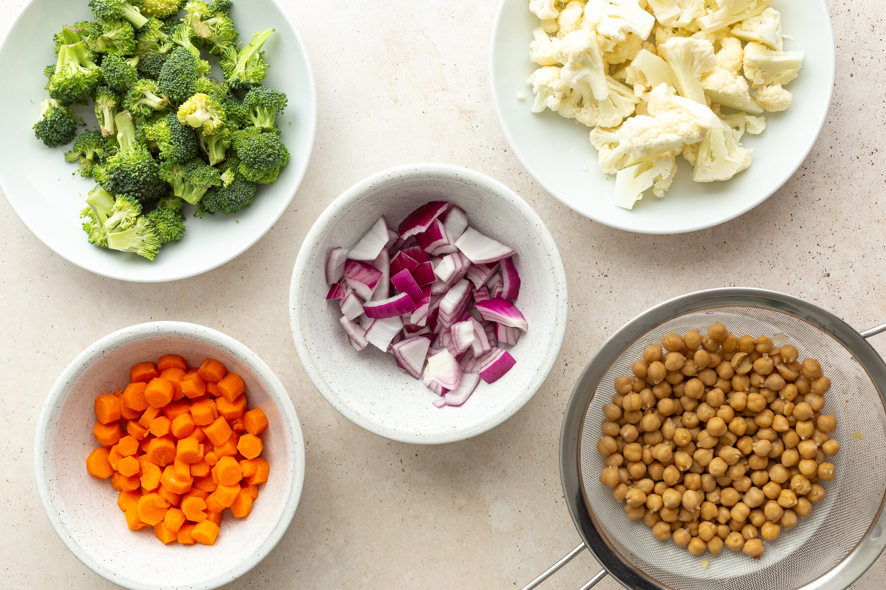 ingredients needed for a roasted veggie bowl: carrots, broccoli, red onion, chickpeas, and cauliflower florets