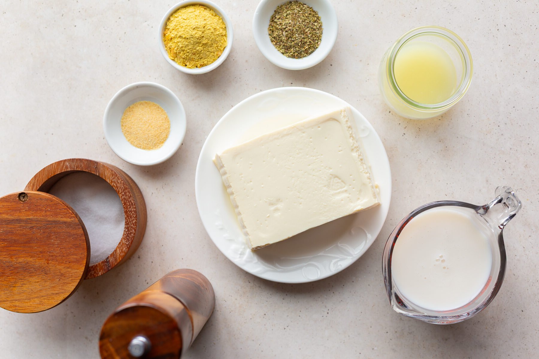 Tofu on a plate near small bowls of seasonings and a glass of milk.