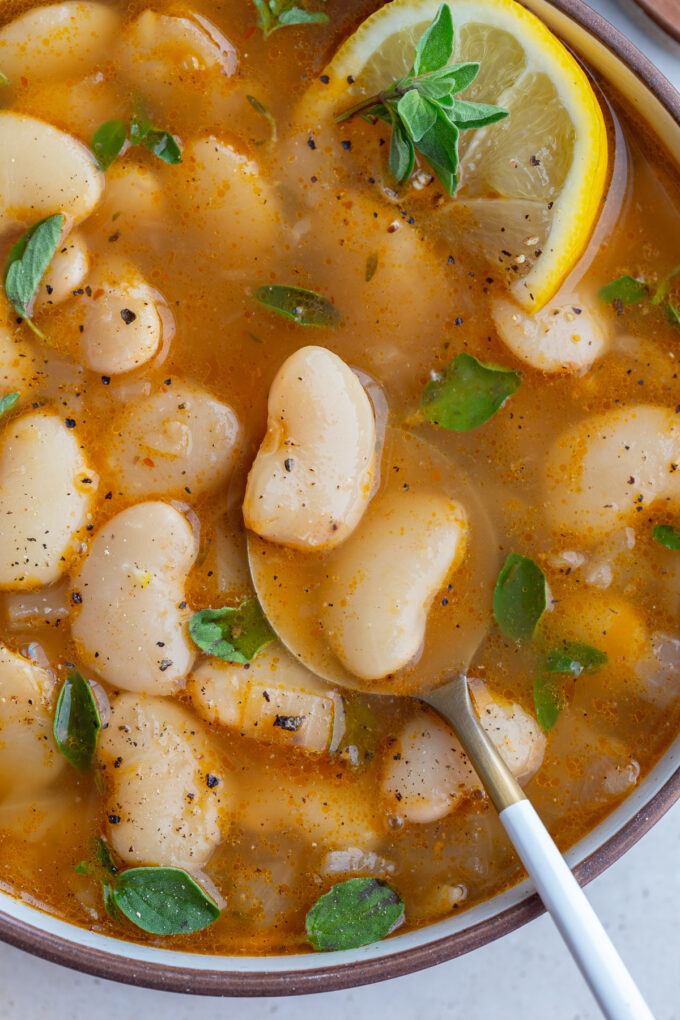 close up shot of brothy beans in a bowl with a spoon and lemon wedge