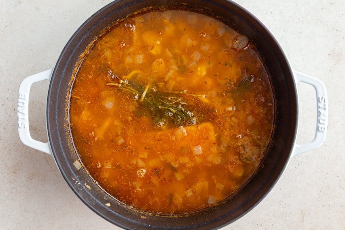 brothy beans in a large pot where you mostly only see the broth and an herb bundle on top