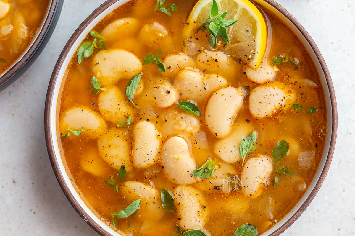 brothy beans in a large bowl with lemon and fresh herbs