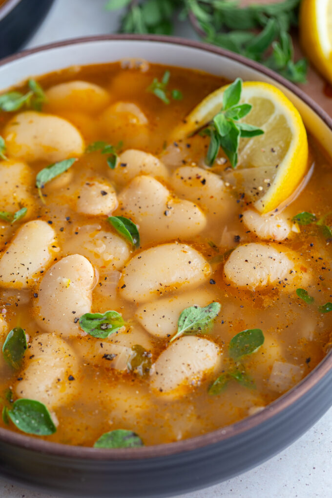 close up shot of brothy beans in a bowl with a lemon wedge