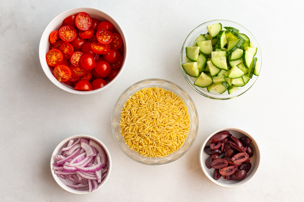 ingredients need for an orzo salad: dried orzo, cherry tomatoes, sliced cucumber, sliced red onion, halved kalamata olives