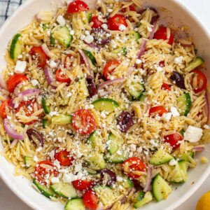 greek orzo salad in a large bowl with cherry tomatoes, kalamata olives, cucumber, red onion and feta