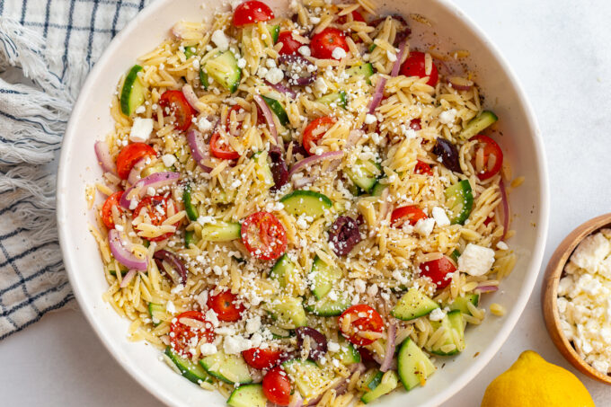 greek orzo salad in a large bowl with cherry tomatoes, kalamata olives, cucumber, red onion and feta