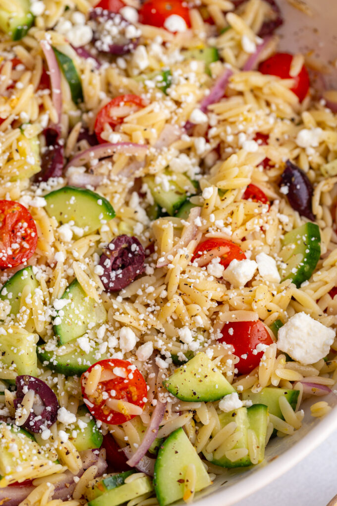 greek orzo salad in a large bowl with cherry tomatoes, kalamata olives, cucumber, red onion and feta