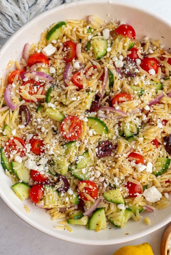 greek orzo salad in a large bowl with cherry tomatoes, kalamata olives, cucumber, red onion and feta