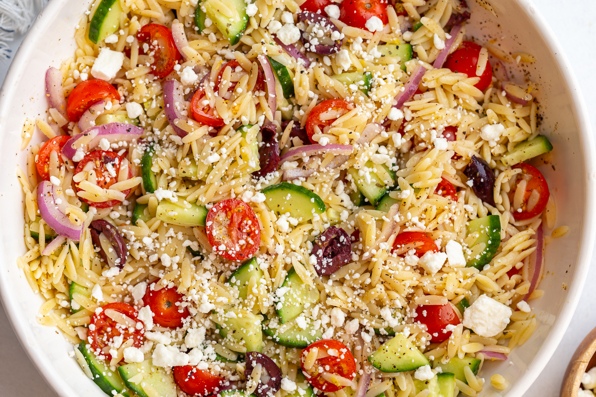 greek orzo salad in a large bowl with cherry tomatoes, kalamata olives, cucumber, red onion and feta