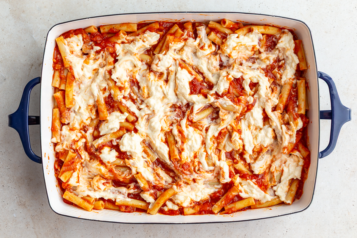 baked ziti being assembled where you see the marinara covered ziti in the casserole dish topped with swirled ricotta