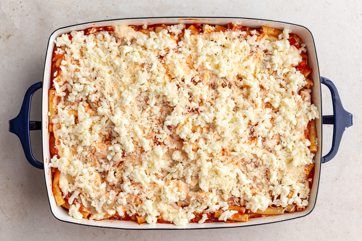 baked ziti in a casserole dish and topped with freshly grated cheese before it has been baked