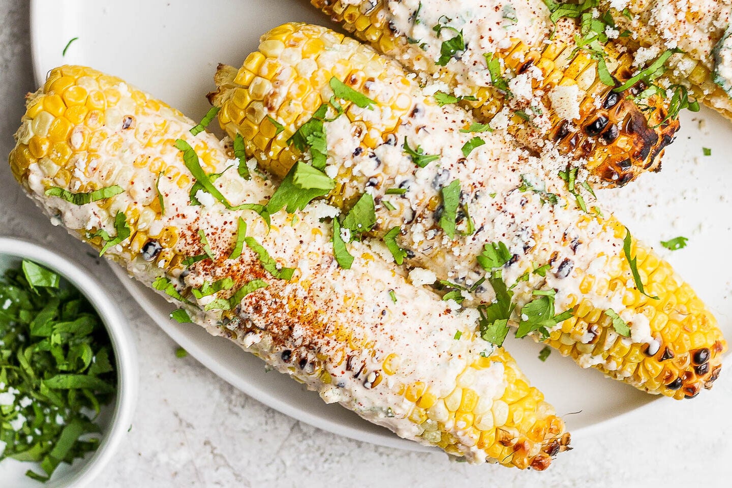 mexican street corn on the cobb on a white plate topped with cilantro and cotija